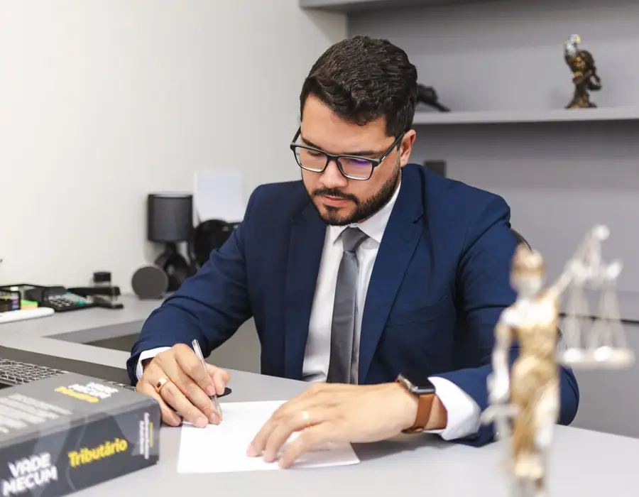 Saulo Romualdo analisando e assinando um documento em sua mesa de trabalho